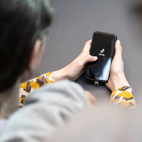 Eine Jugendliche schaut auf ein Handy mit TikTok-Logo - nach einer TikTok-Challenge ist eine Schülerin aus Kaiserslautern ins Krankenhaus gekommen.