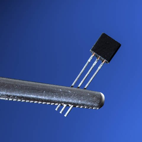 Ein elektronischer Transistor wird von einer Pinzette gehalten.